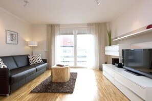 Ein modernes Wohnzimmer mit einer Couch, einem Couchtisch, einem Flachbildfernseher und einem großen Fenster mit Vorhängen.