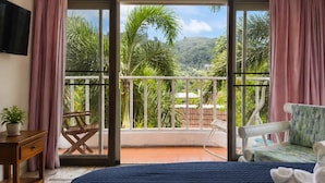 Un dormitorio con una cama grande, un escritorio, una silla y un balcón con vistas a zonas verdes y una montaña.