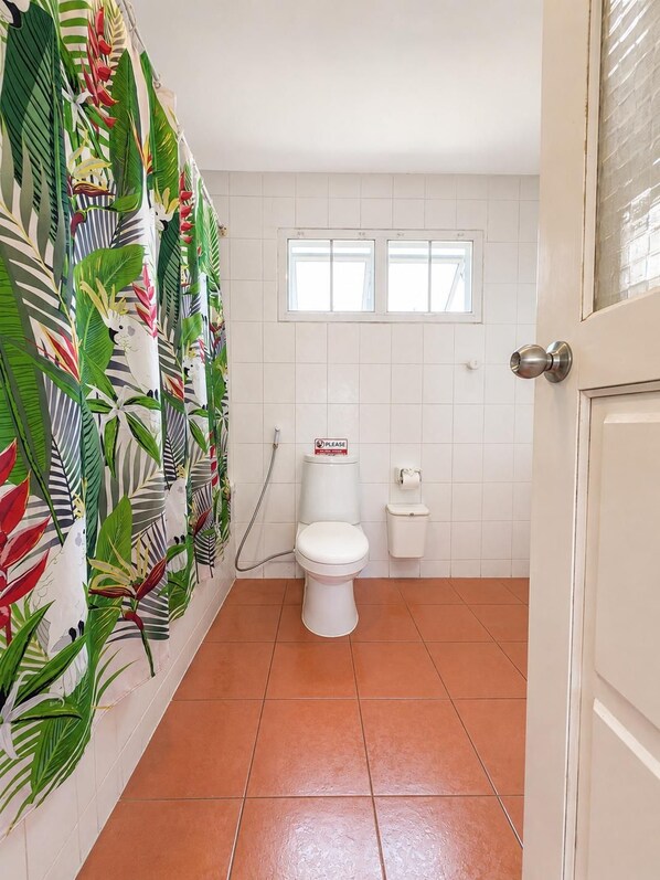 Een badkamer met toilet, douche en een raam.