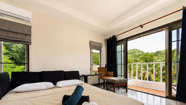 Habitación de hotel con una cama grande, una silla y un balcón con vistas a zonas verdes.