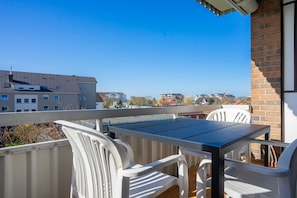 Un balcón al aire libre con una mesa y sillas, con vistas a una zona residencial con edificios y cielo despejado.