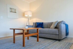 Ein Zimmer mit einer Couch, einem kleinen Holztisch, einer Lampe und einem gemusterten Teppich.
