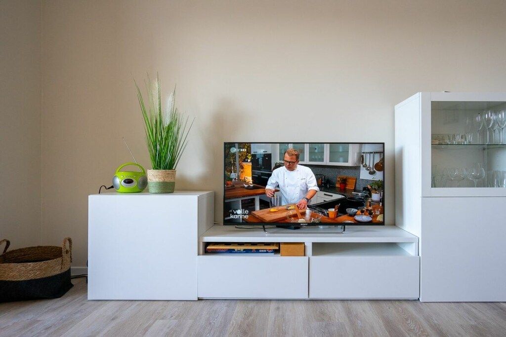 A modern kitchen with a flat-screen TV on a white cabinet, a green speaker, and a potted plant.