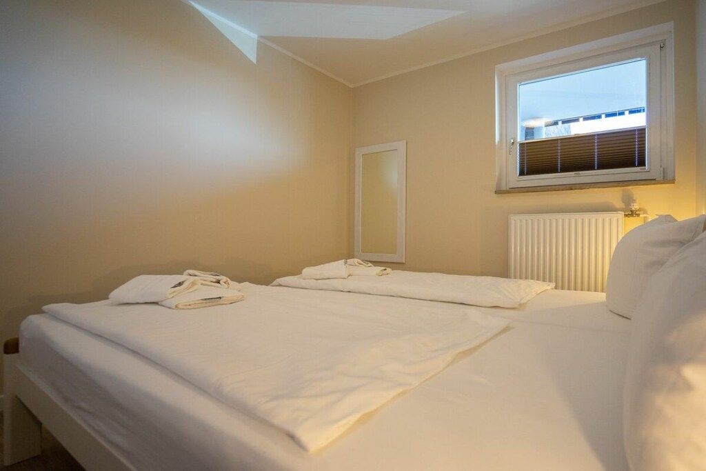 A hotel room with two beds, a window with blinds, a radiator, and a mirror on the wall.