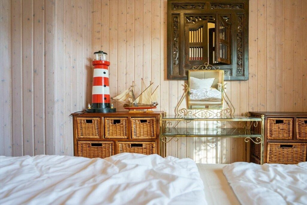 A room with a bed, a desk with wicker baskets, a mirror, and a decorative lighthouse.