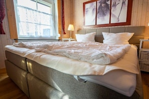 A neatly made bed with a grey headboard, a bedside table with a lamp, and a window with curtains. - Holiday home in Büsum with swimming pool (Büsum)