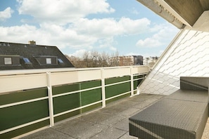 A rooftop terrace with a green safety barrier, a white railing, and a wicker sofa. - Holiday apartment in Büsum with swimming pool (Büsum)