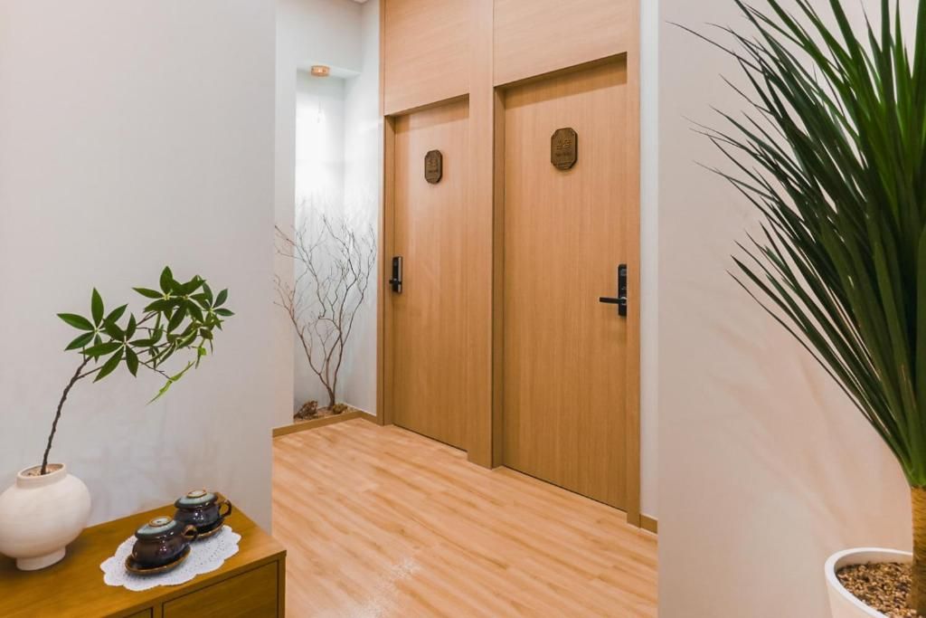 A hallway with wooden doors, a small table with a plant and teapots, and a potted plant on the right.