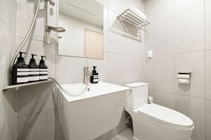 A modern bathroom with a white sink, toilet, and shower. There are three bottles of shampoo, conditioner, and body wash on the sink. - SO ON Stay (Seoul)