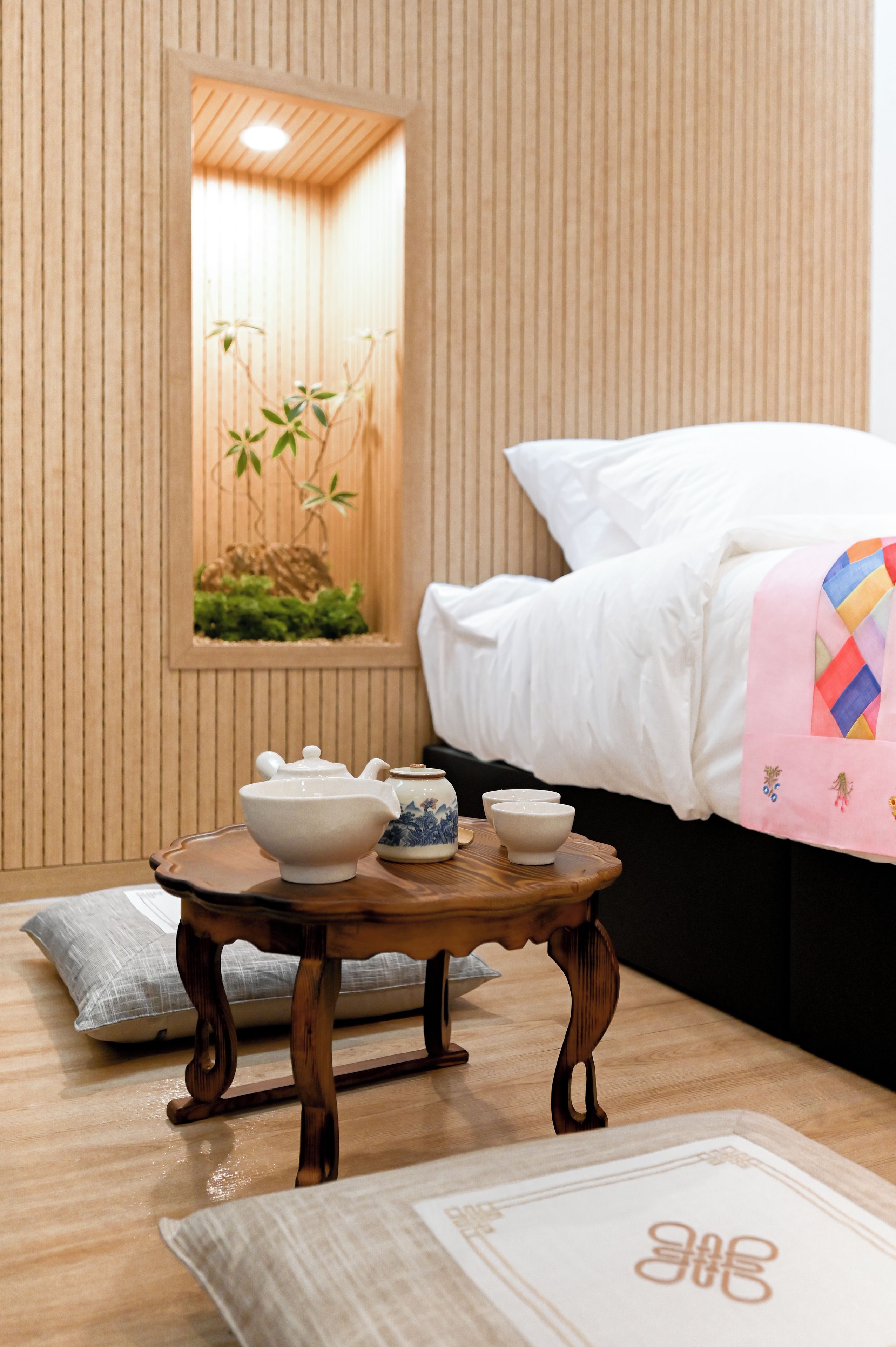 A room with a bed, a small wooden table with teacups, a decorative wall panel, and a framed picture of bamboo.