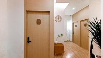 Un pasillo con piso de madera, una puerta con cerradura digital, un pequeño banco de madera con una planta y un reloj de pared.