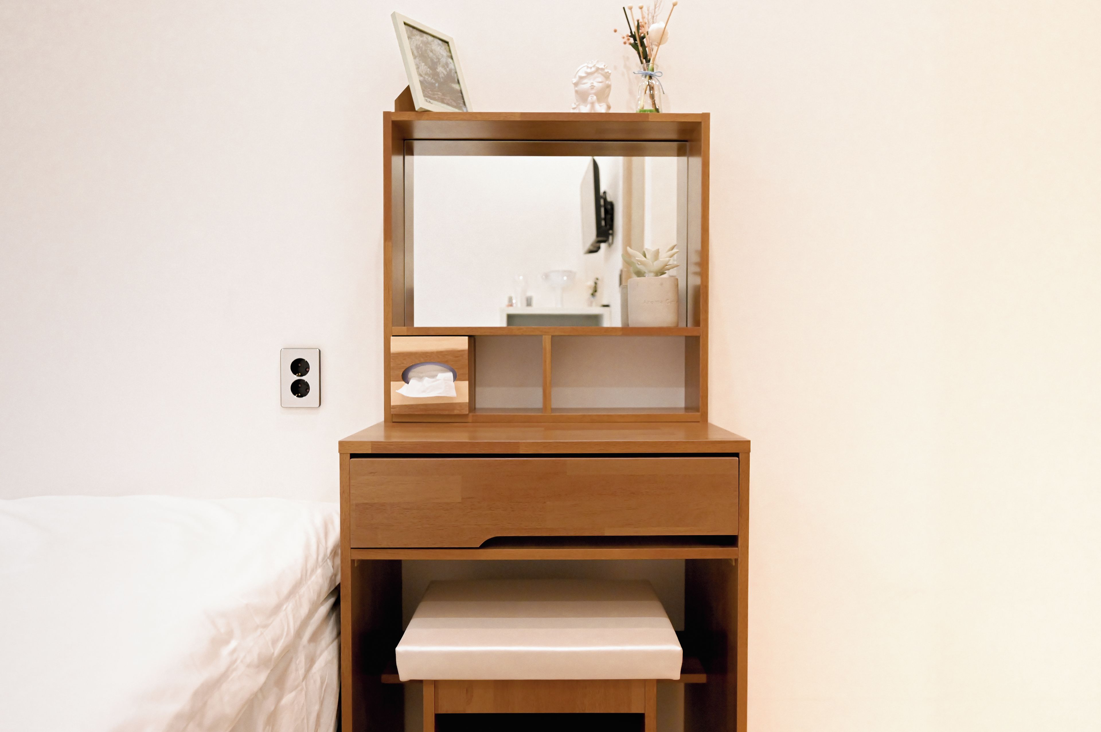 A wooden bedside table with a mirror, a small shelf with a picture frame, and a tissue box.