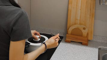 A person using a kitchen appliance, possibly a rice cooker, on a countertop with a wooden cutting board nearby.