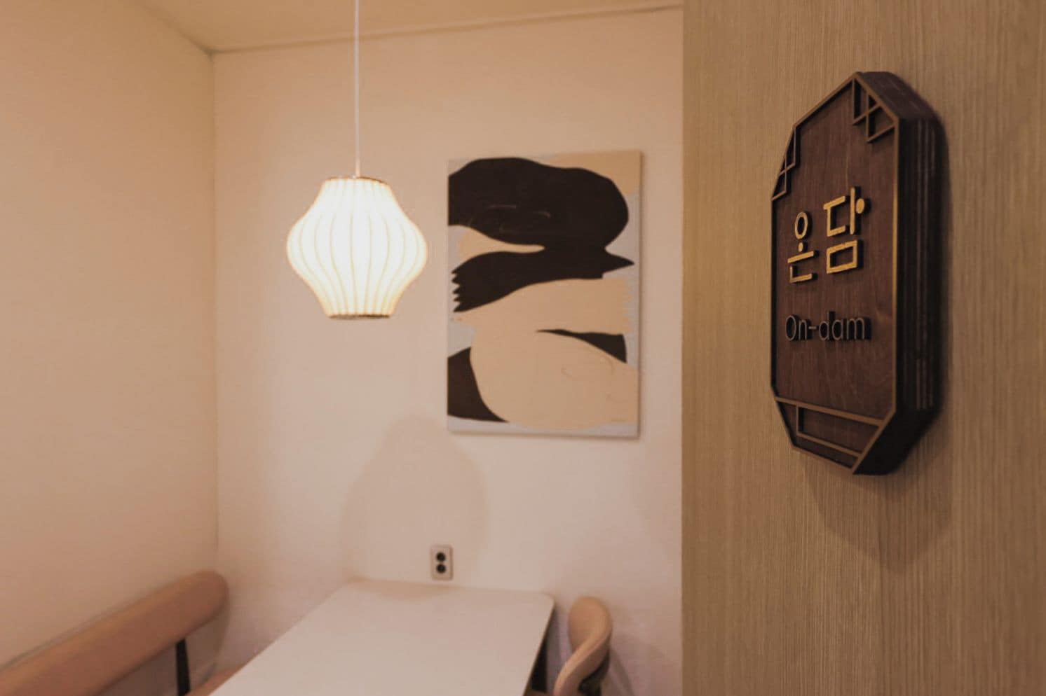 Una habitación con un letrero de madera montado en la pared, una lámpara colgante y una obra de arte abstracta.