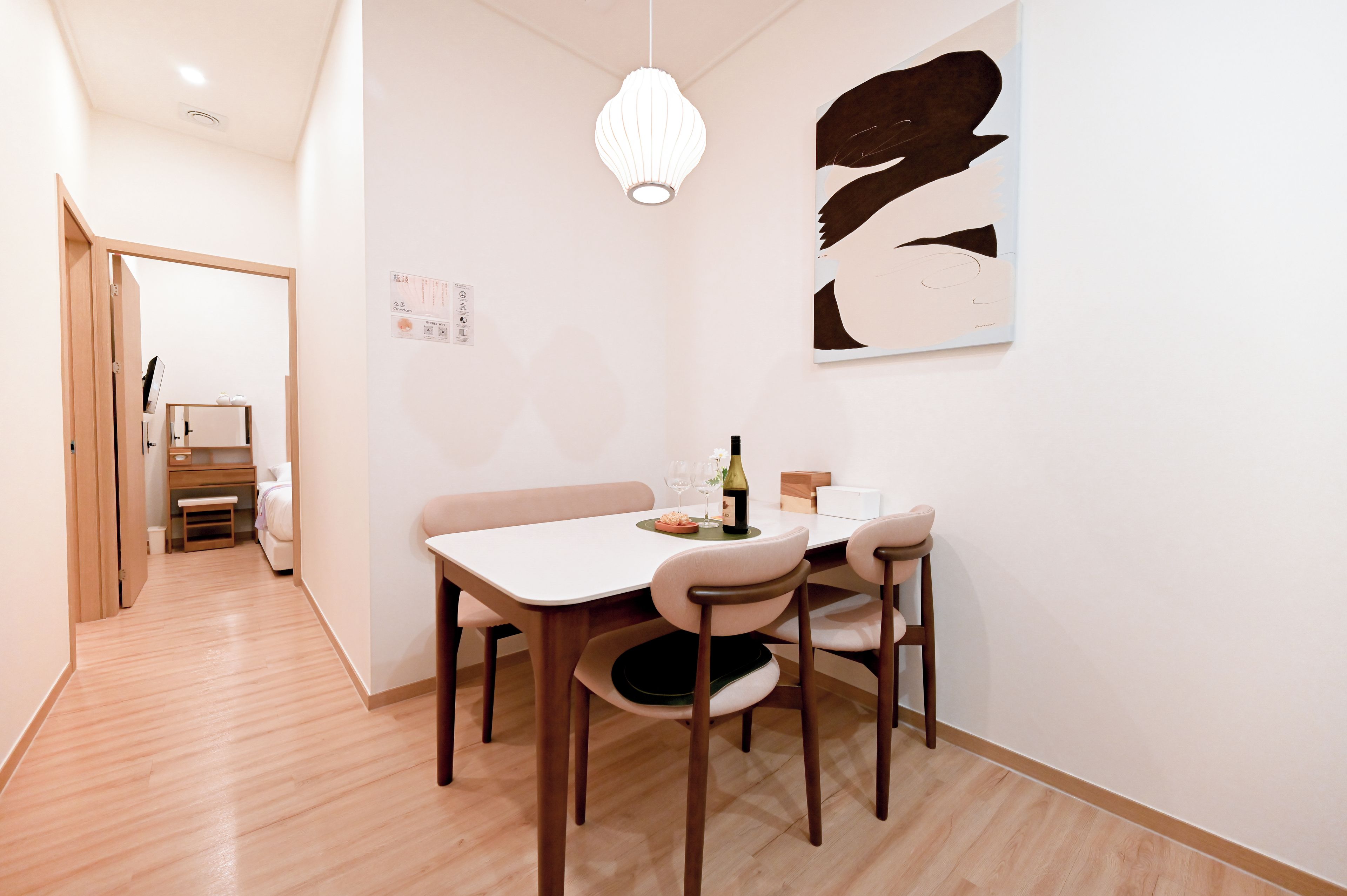 A modern dining area with a white table, four chairs, a hanging light fixture, and a wall-mounted abstract artwork.