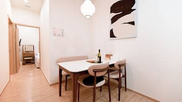 A modern dining area with a white table, four chairs, a hanging light fixture, and a wall-mounted abstract artwork.