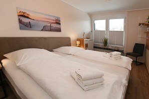 Ein Hotelzimmer mit zwei Betten, einem Bild an der Wand, einem Fenster mit Jalousien und einem Sessel.