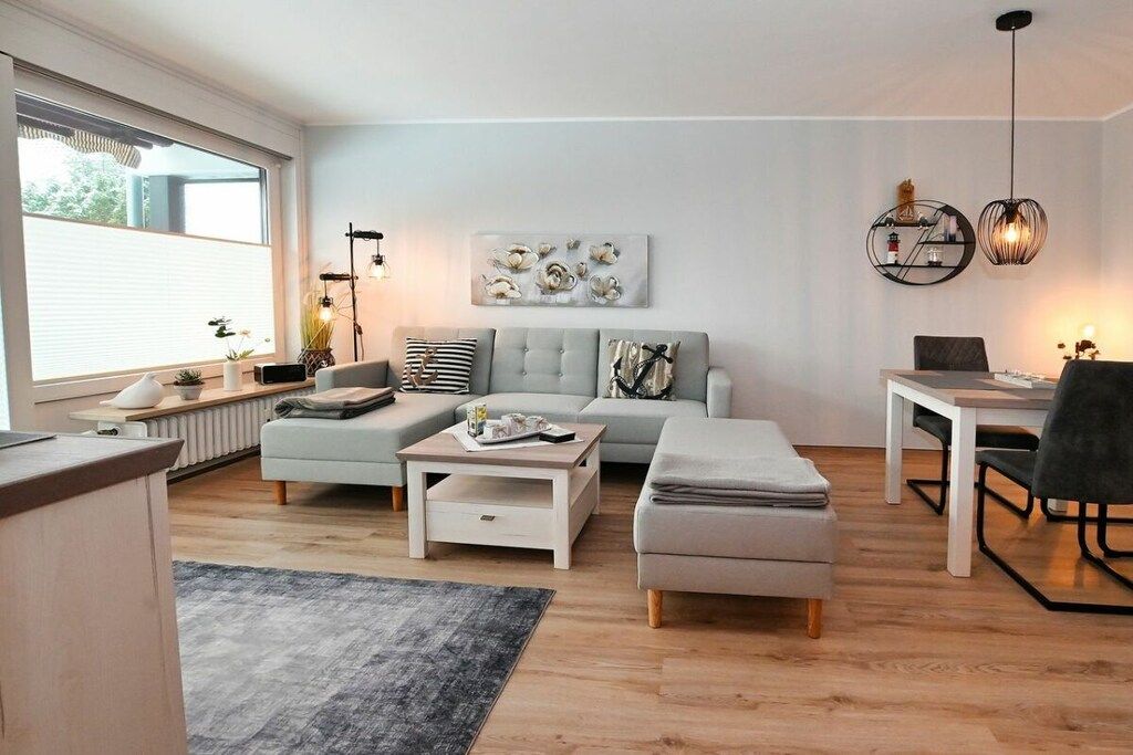 Ein modernes Wohnzimmer mit einer Couch, einem Hocker, einem Couchtisch und einem Essbereich mit Tisch und Stühlen.