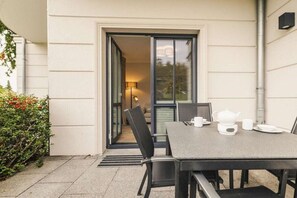 Eine Terrasse im Freien mit Tisch, der für ein Kaffeetrinken gedeckt ist, einem Stuhl und einer Tür zu einem Innenraum.