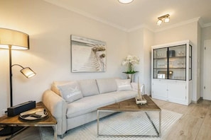 A modern living room with a sofa, coffee table, lamp, artwork, and a cabinet. - Logierhaus Friedrich WE 2 (Zingst (Ostseeheilbad))