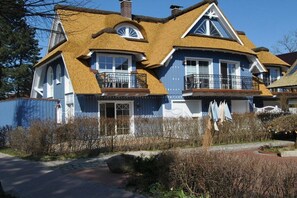 A two-story house with a unique thatched roof, large windows, and a balcony. - Evening - Apartment 4 (Zingst (Ostseeheilbad))