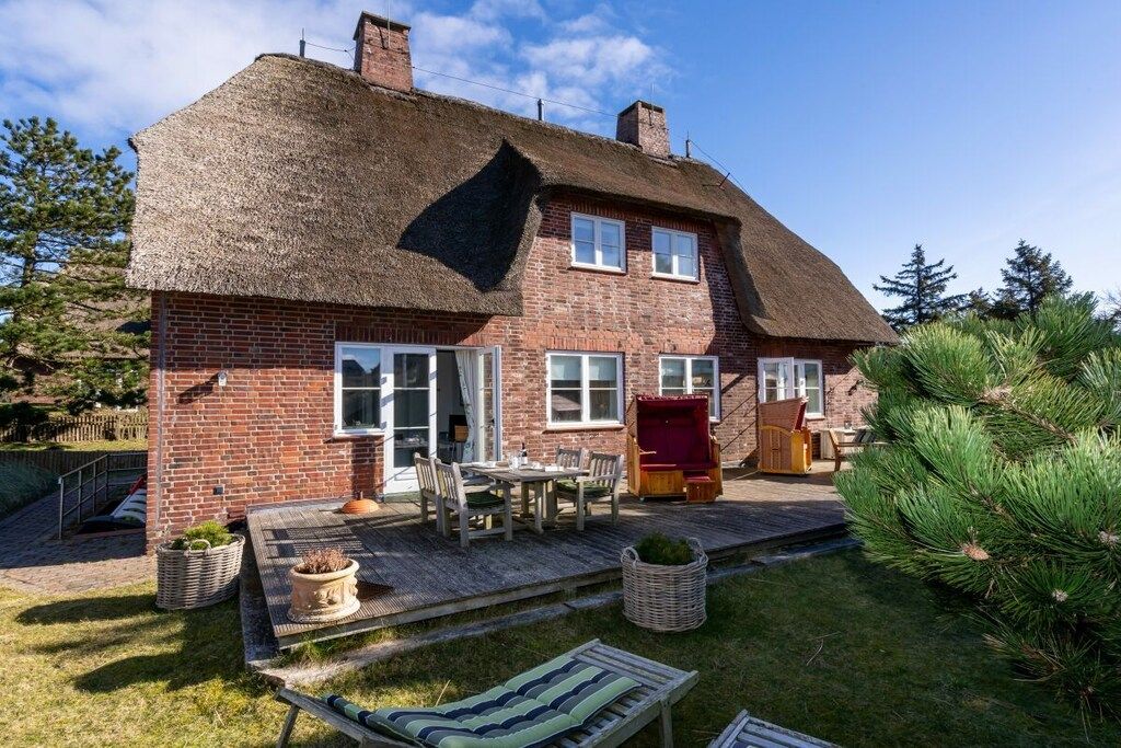 Una casa de ladrillo con tejado de paja, un patio con mobiliario exterior y un pequeño jardín.