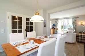 A dining area with a wooden table set for four, white chairs, and a hanging light fixture. - Holiday home with 1 bedroom (List auf Sylt)
