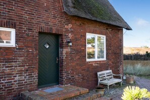 A brick house with a green door, a window, and a bench outside. - Holiday home with 1 bedroom (List auf Sylt)