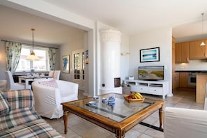 A living room with a sofa, a coffee table, and a television. There is a kitchen area with cabinets and a countertop. - Holiday home with 1 bedroom (List auf Sylt)