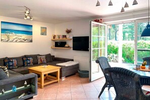 Un salon avec un canapé, une table basse et un téléviseur. Une fenêtre offre une vue sur la verdure à l’extérieur.