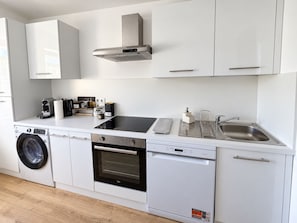 A compact kitchen with a washing machine, oven, dishwasher, and a sink with a soap dispenser. - Stella Rosa Vacation Rental — Private, air-conditioned apartment with self-check-in (Soleuvre)