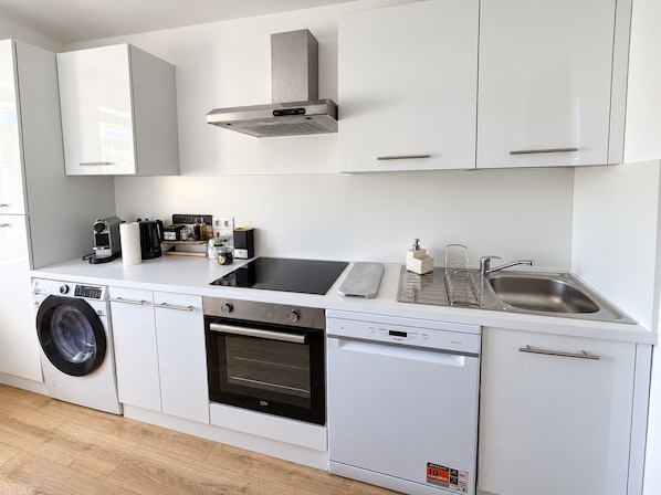 A compact kitchen with a washing machine, oven, dishwasher, and a sink with a soap dispenser.
