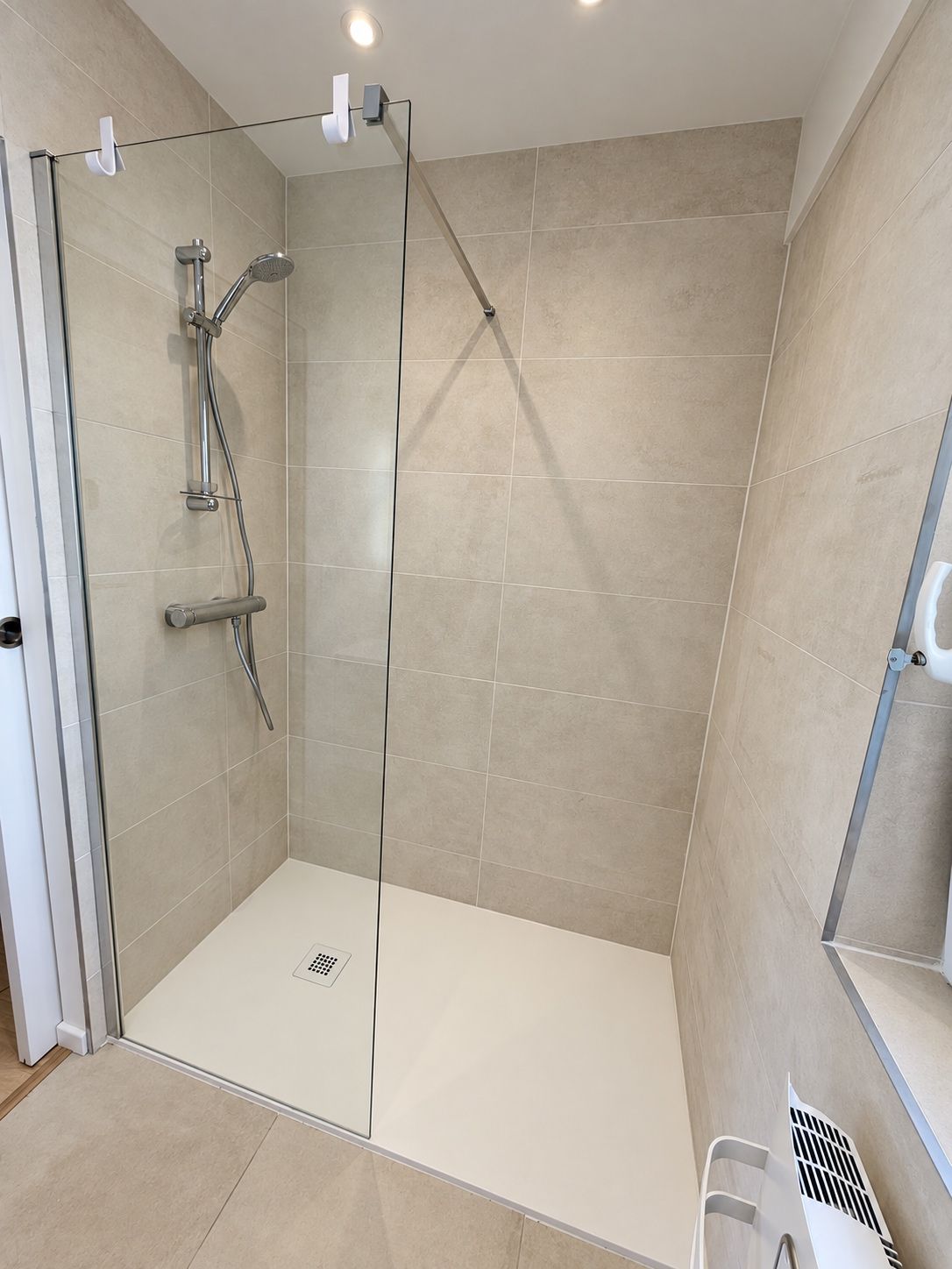 Eine moderne Dusche mit Glastür, Handbrause und am Wand montiertem Wasserhahn.
