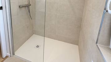 Eine moderne Dusche mit Glastür, Handbrause und am Wand montiertem Wasserhahn.