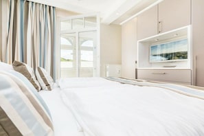 Ein Hotelzimmer mit Bett, Fernseher, einem Fenster mit Vorhängen und Blick ins Freie.