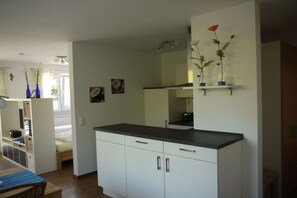 A compact kitchen with white cabinets, a black countertop, and a mirror above. There are two blue vases with flowers on a shelf. - House of Four Elements (Zinnowitz)