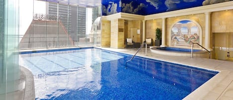 An indoor swimming pool with a clear view of the surrounding area, including a seating area and a mural on the wall.