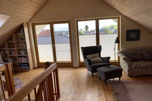 A room with a sloped ceiling, a bookshelf, a black armchair, a patterned sofa, and a wooden floor. - Holiday home with 1 bedroom (Maasholm Bad)