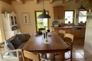 A wooden dining table with chairs, a hanging light fixture, a cabinet, and a window with a view of greenery. - Holiday home with 1 bedroom (Maasholm Bad)