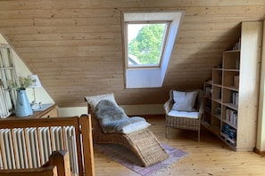 A cozy room with a sloped ceiling, a window, a wicker chair, a bookshelf, and a radiator. - Holiday home with 1 bedroom (Maasholm Bad)