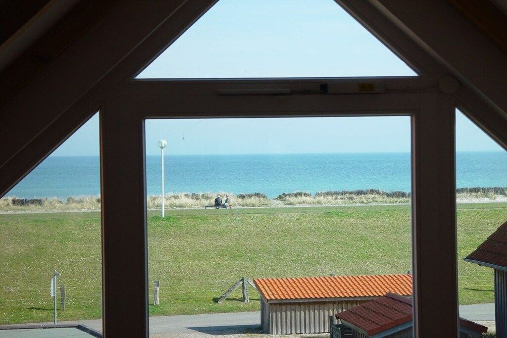 A view through a window of a grassy area with a building and a body of water in the distance.