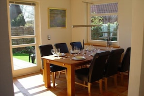 Ein Essbereich mit einem Holztisch, gedeckt für sechs Personen, sechs Stühlen und Blick auf den Garten durch große Fenster.