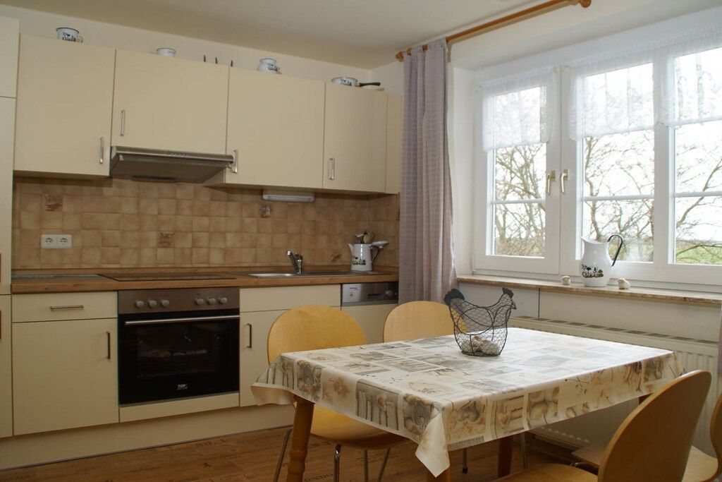 Una cocina compacta con comedor, una ventana con cortinas y una mesa con mantel estampado.