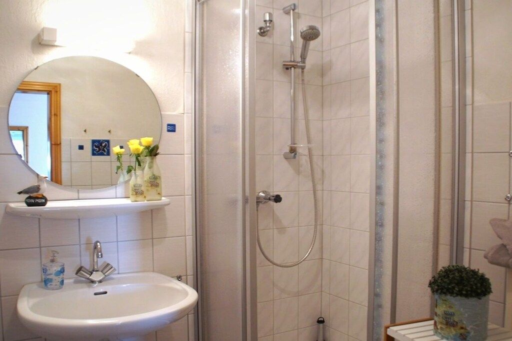 Un baño con un lavamanos blanco, un espejo, cabina de ducha y un estante pequeño con artículos de tocador.
