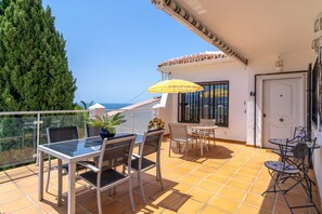 A balcony with a glass table and chairs, a yellow striped umbrella, and a view of the sea. - Holiday Home in Nerja With Sea Views (Nerja)