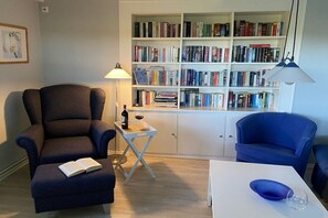 Un salon comprenant une bibliothèque, un fauteuil de lecture, une petite table avec un livre et une lampe.