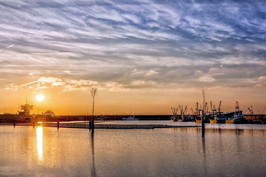 A harbor at sunset with boats docked, a pier, and a lighthouse.