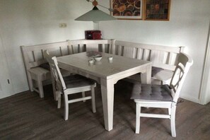 A dining area with a white table and benches, a pendant light, and a framed picture on the wall. - Holiday apartment Hell (Wesselburener Deichhausen)