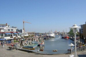 Un port de plaisance avec des bateaux amarrés, une grue en arrière-plan et une promenade piétonne longeant l’eau.