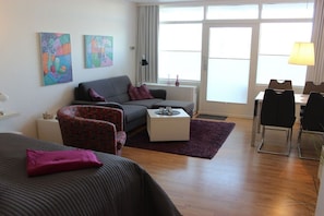 A modern hotel room with a sofa, armchair, coffee table, and a dining area with chairs. - Holiday apartment with 2 bedrooms (Fehmarn)